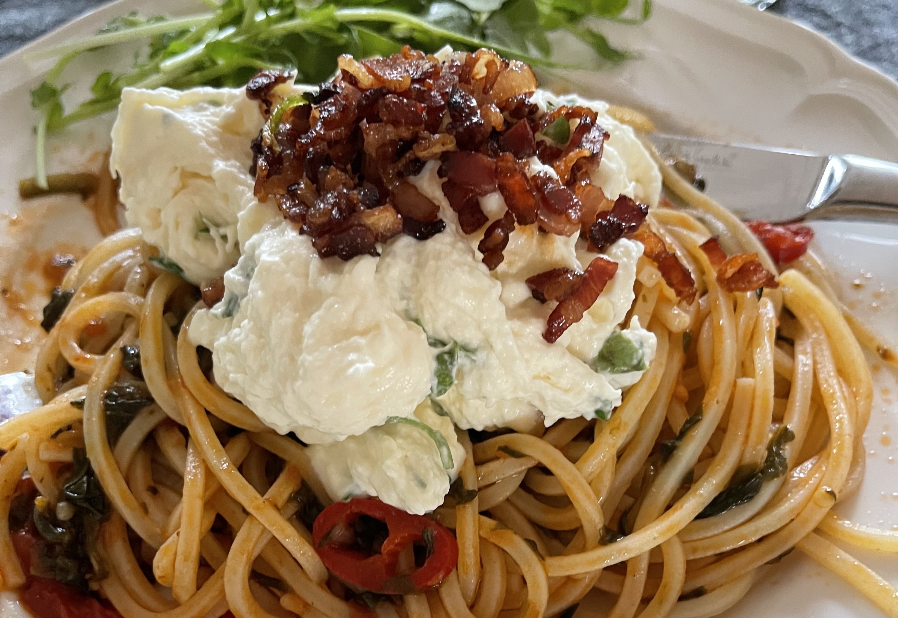 A plate of spaghetti and layers of Burrata and bacon
